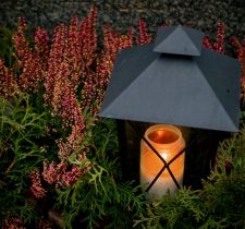 Una candela commemorativa accesa in una lanterna tra i fiori – Agenzia funebre Haron