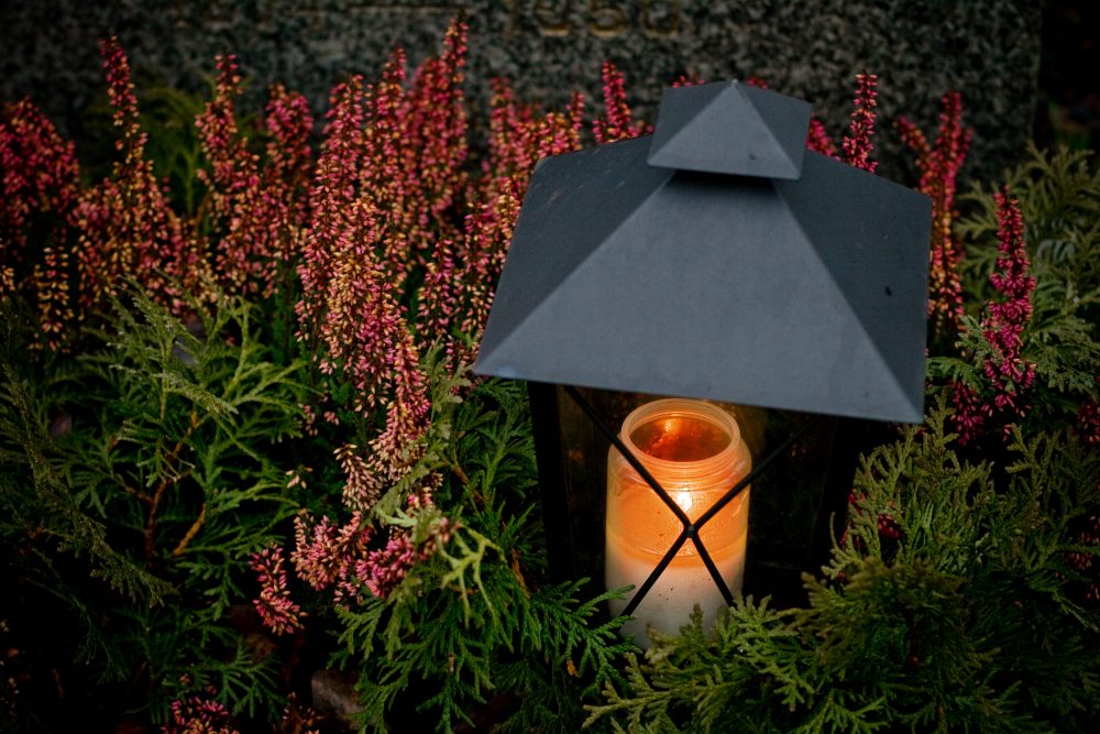 A lit memorial candle in a lantern among flowers – Haron Funeral Agency