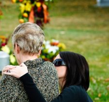 Woman embracing and comforting a grieving person in a cemetery