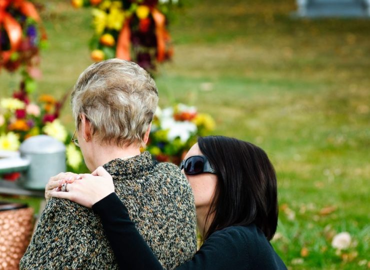 Woman embracing and comforting a grieving person in a cemetery