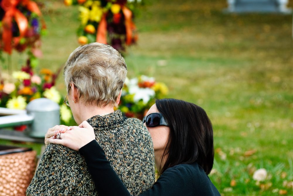 Woman embracing and comforting a grieving person in a cemetery