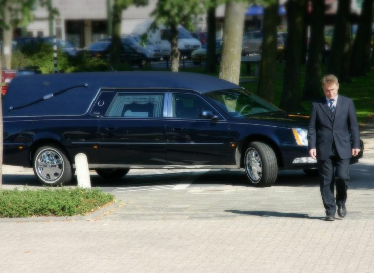 Black hearse with a funeral attendant standing beside it