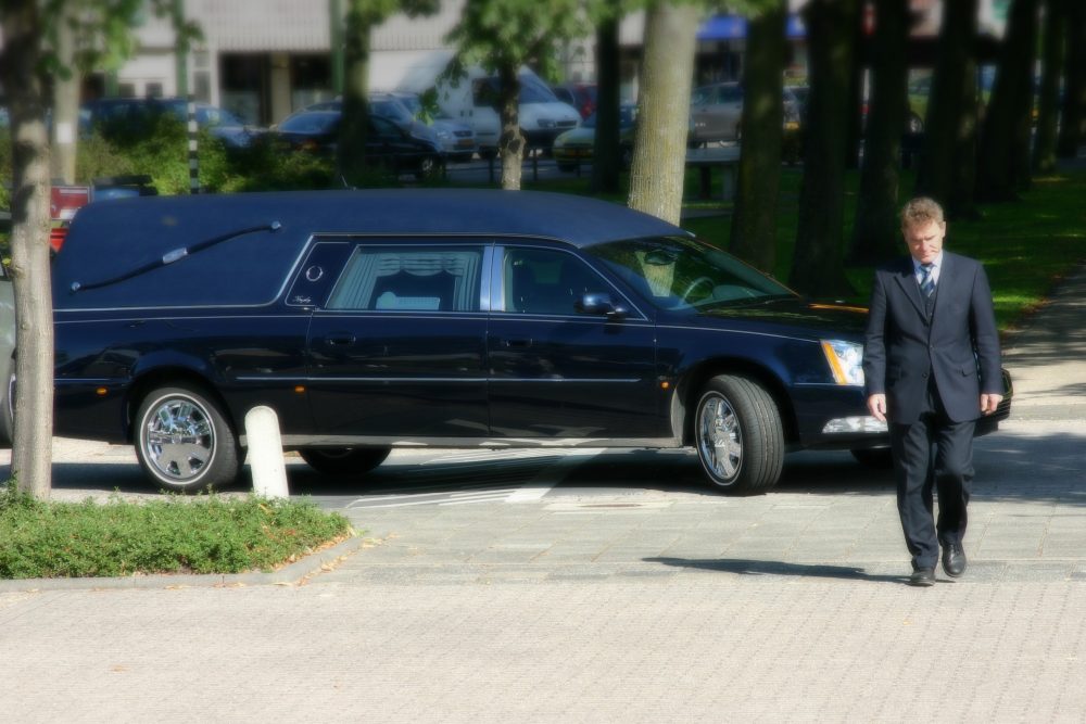 Black hearse with a funeral attendant standing beside it