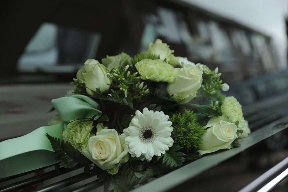 Arrangement of white roses and gerberas displayed on a funeral vehicle