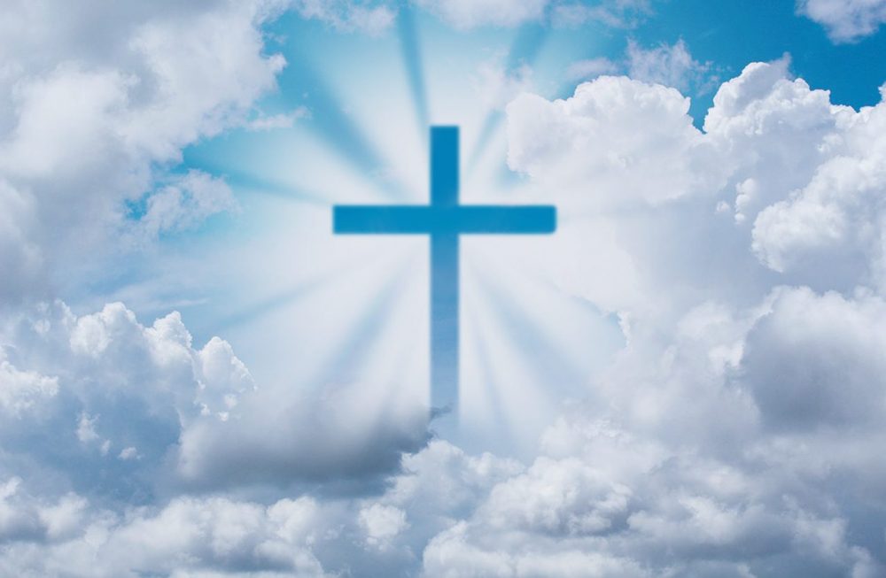 Christian cross illuminated by light among heavenly clouds